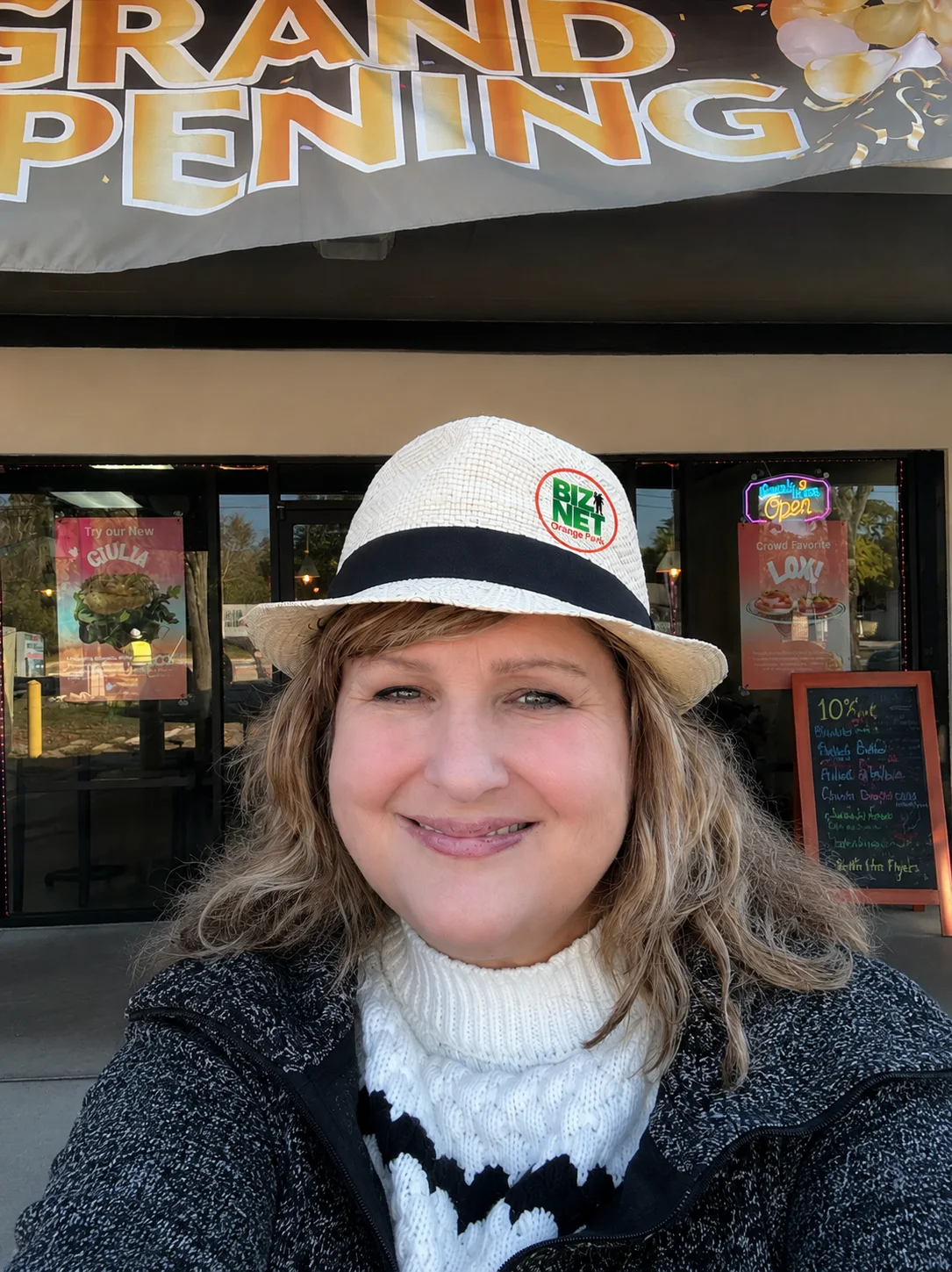 A local business owner smiling in front of her storefront under a Grand Opening banner